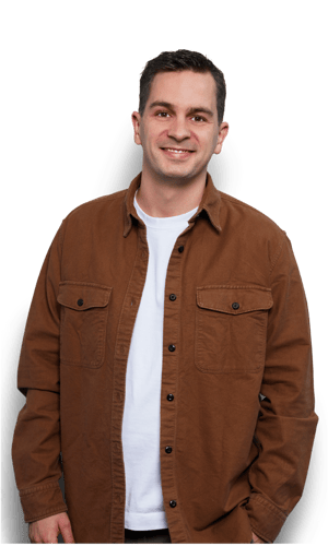 Smiling man in a brown jacket and white shirt, standing against a white background. Casual attire, friendly expression.