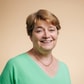 Een lachende vrouw in een groene trui poseert voor een beige achtergrond.