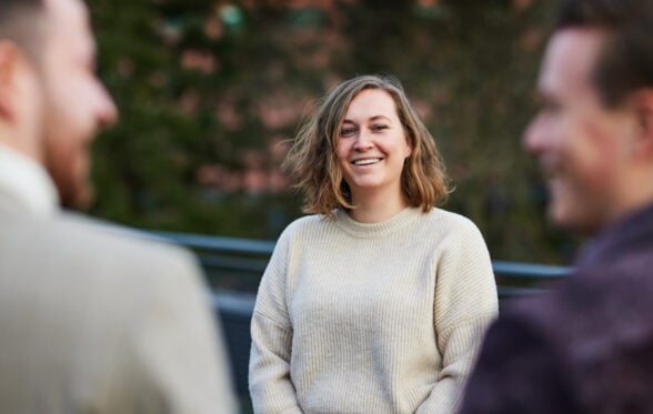 Person smiles at colleagues during casual conversation outside on a sunny day.