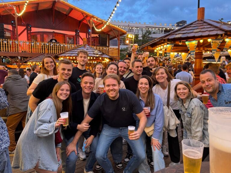 Groep vrienden geniet van avondje uit op een druk, sfeervol oktoberfest met muziek en verlichting.