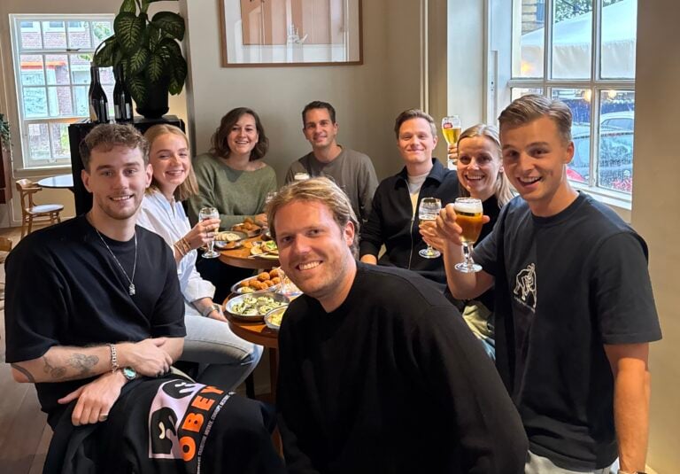 Groep vrienden geniet van een gezellig diner in een restaurant, proostend met drankjes en lachend rondom de tafel.