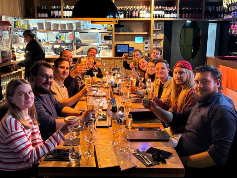 Groep vrienden proost in een gezellig restaurant onder warme verlichting, met chefs actief in de open keuken.